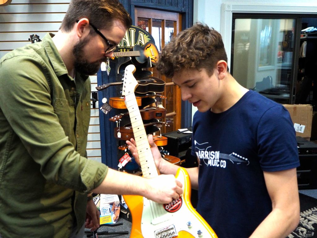Student holding guitar in music shop